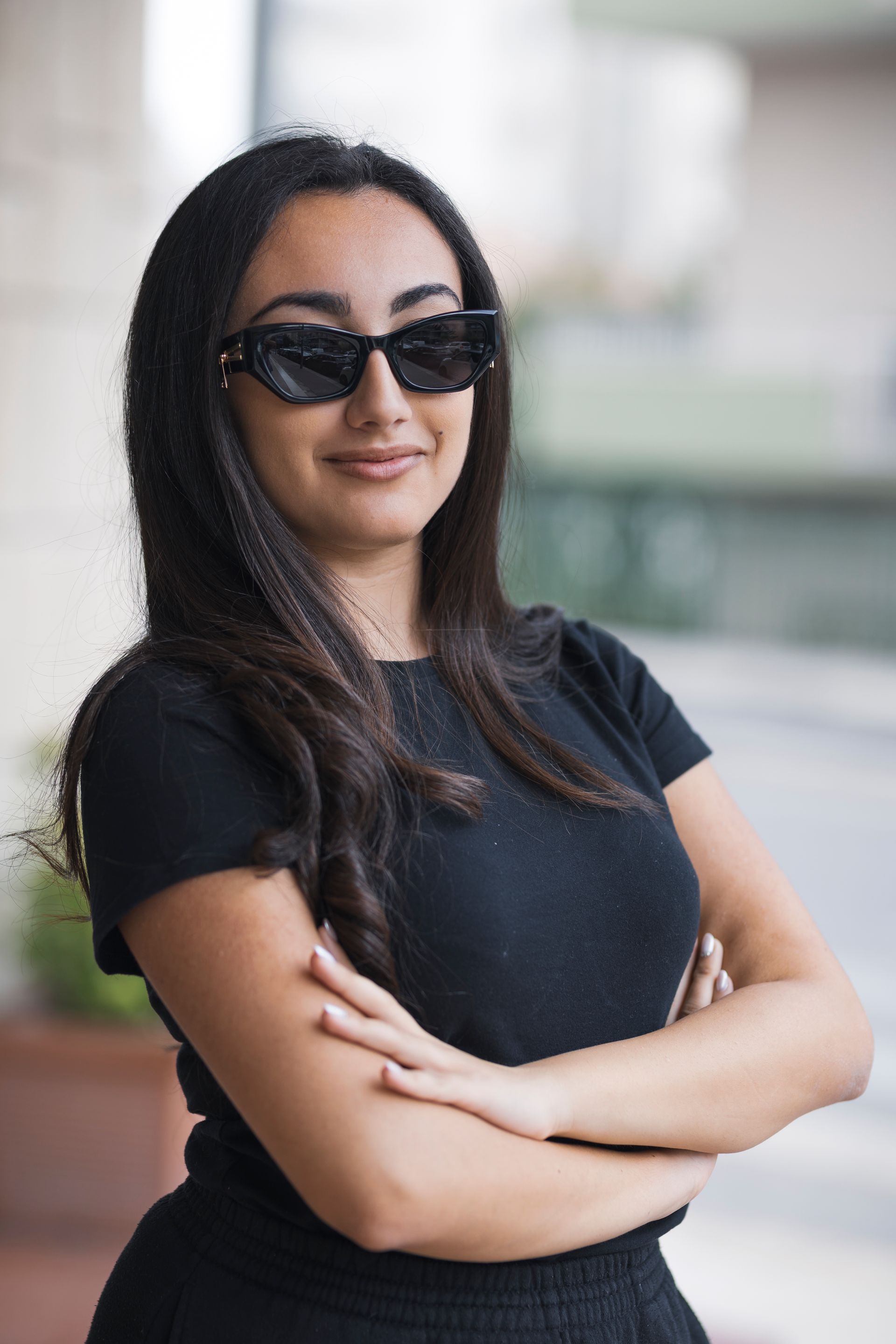 Una donna che indossa occhiali da sole e una maglietta nera è in piedi con le braccia incrociate.