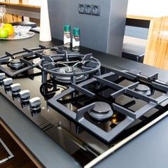 Black gas cooktop with dark gray grates and knobs, in a modern kitchen.