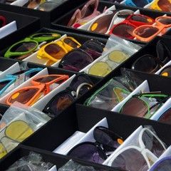 Sunglasses displayed in black trays, various colors, for sale.