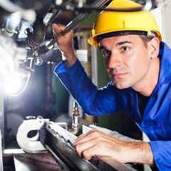 Man in yellow hard hat and blue work shirt working on machinery.