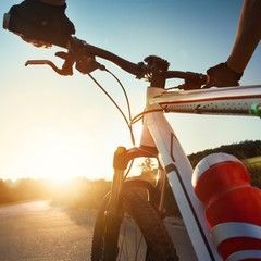 Bicyclist riding on a road towards the sun; bike frame and handlebars visible; water bottle attached.