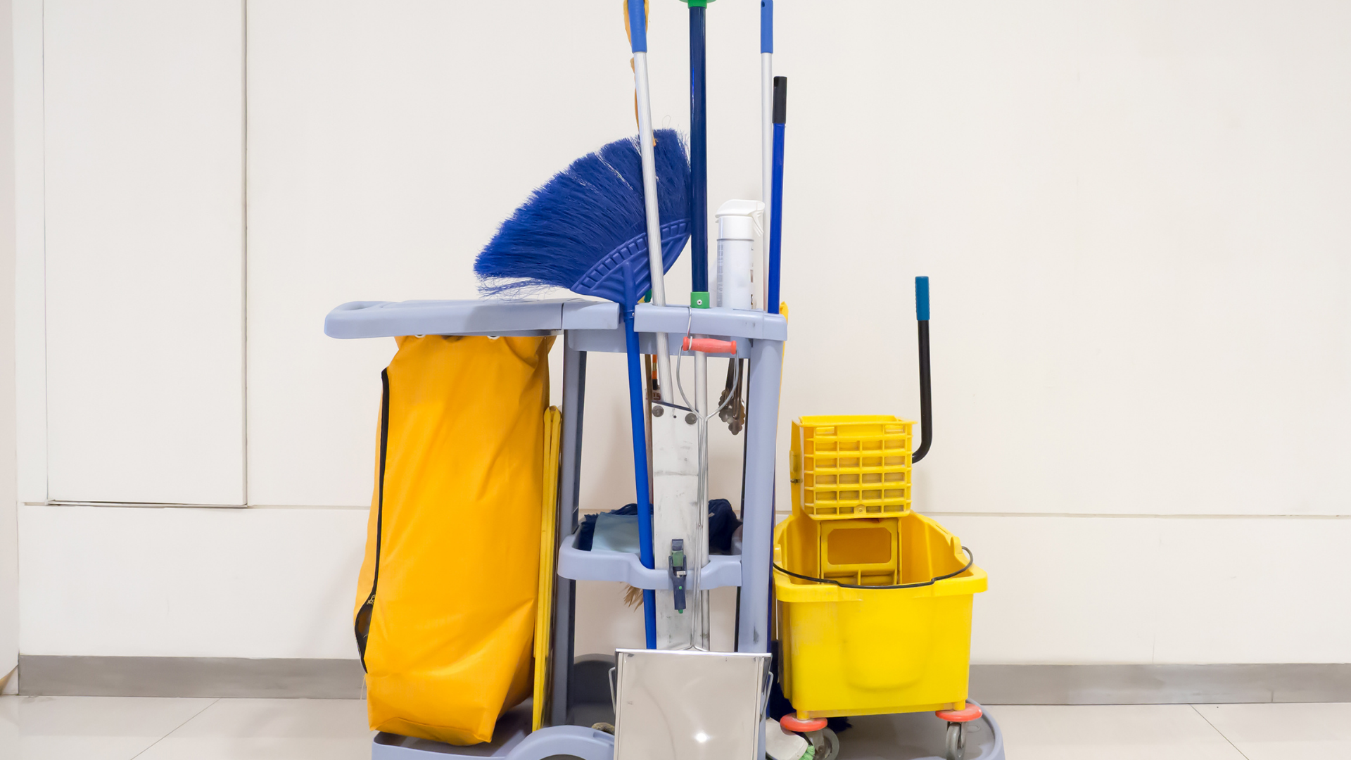 Yellow mop bucket with wringer and mop handle, against a dark background.