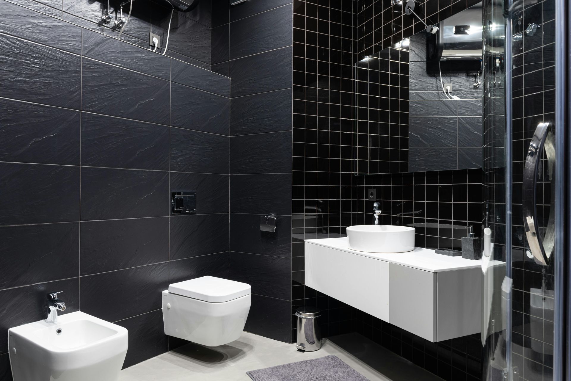 A bathroom with black tiles and white sinks and toilets