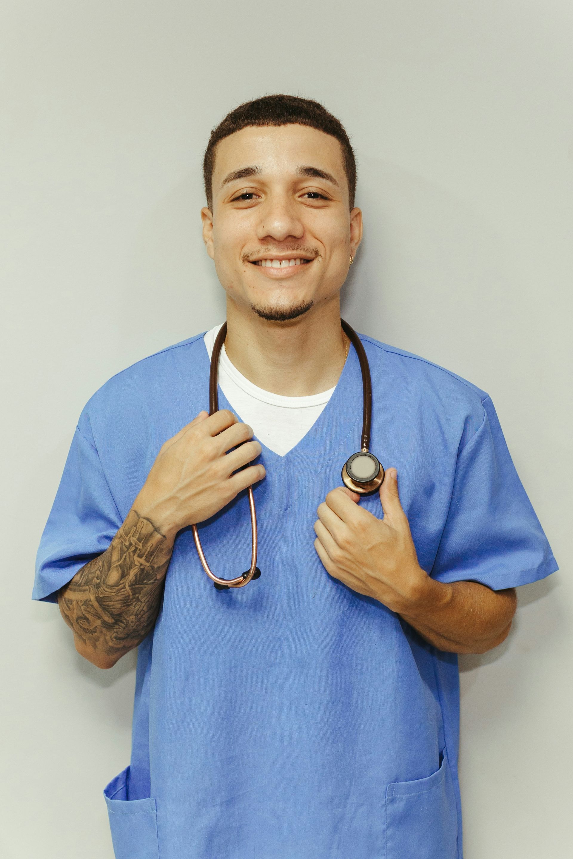 A man in a blue scrub is holding a stethoscope around his neck