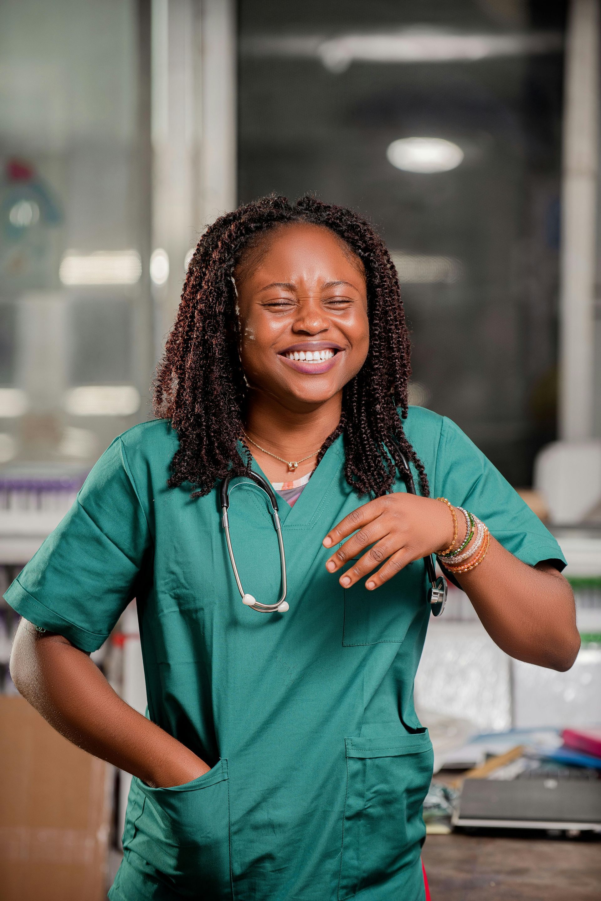 A woman in a green scrub top with a stethoscope around her neck is smiling.