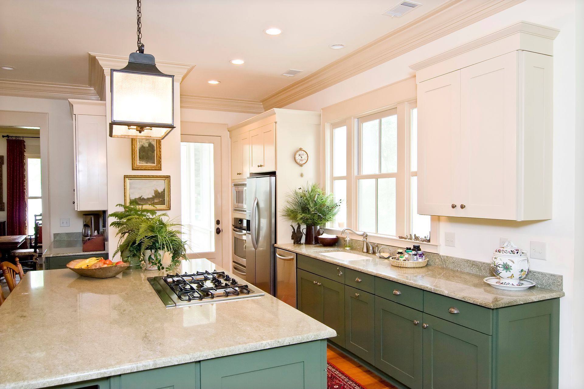 Kitchen with sage green cabinets, light countertops, and large island with cooktop, centered under a hanging lantern.