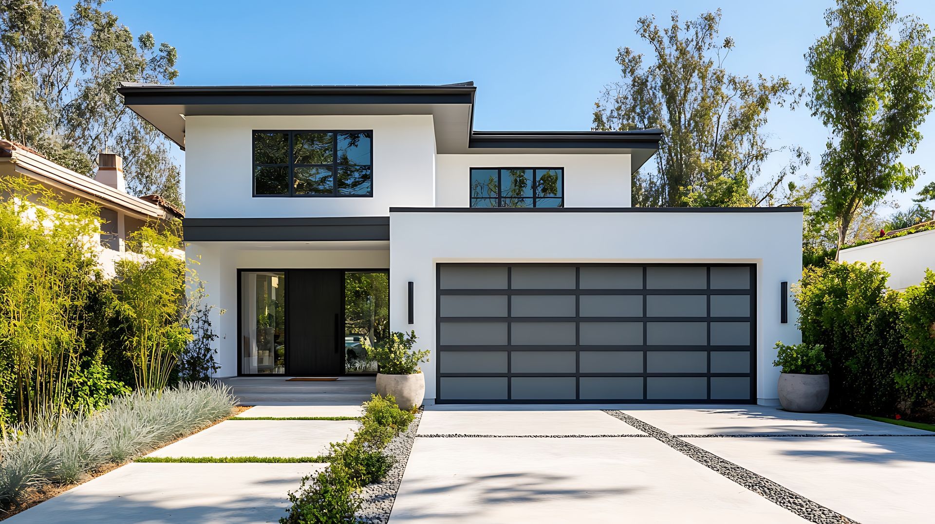 Modern white two-story house with a gray garage door and a concrete driveway lined with greenery.