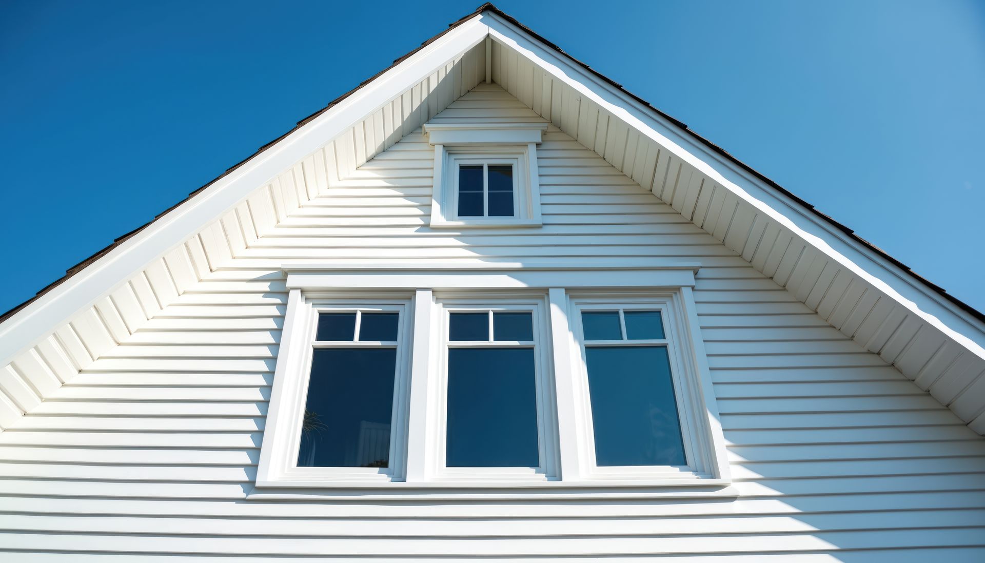 White house gable with windows against a clear blue sky.