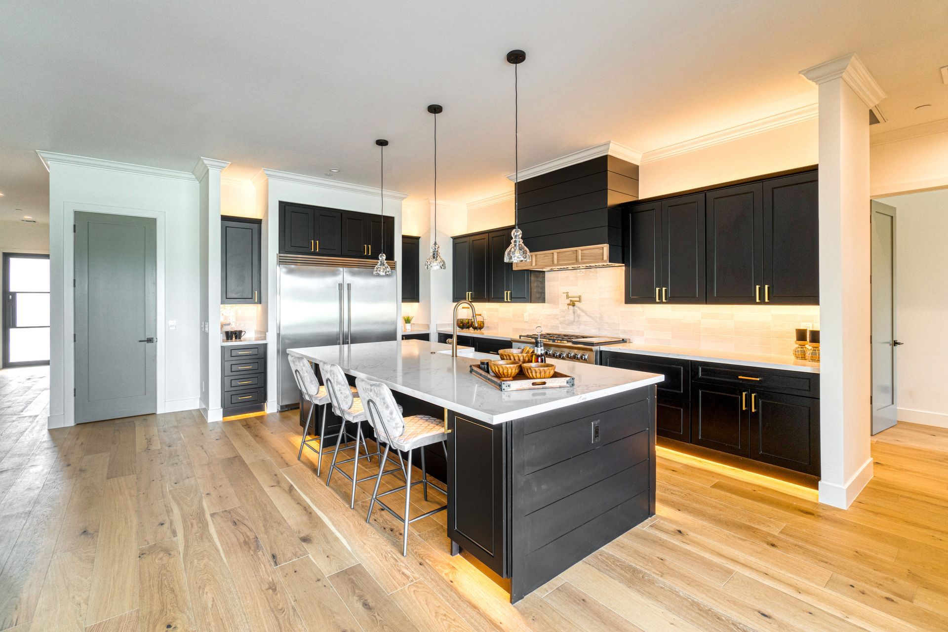 Modern kitchen with black cabinets, white island with stools, stainless steel appliances, and wood floors.