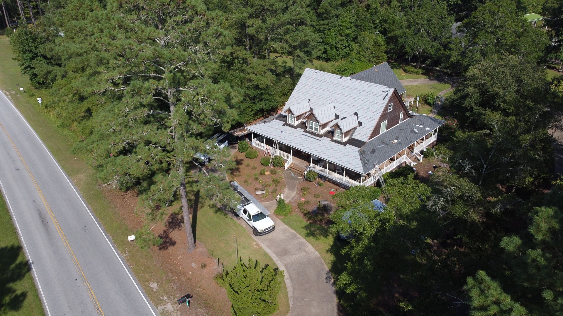 An aerial view of a house next to a road surrounded by trees.
