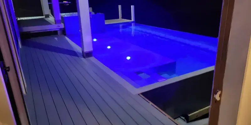 Night view of pool and hot tub beside completed composite deck with blue lighting