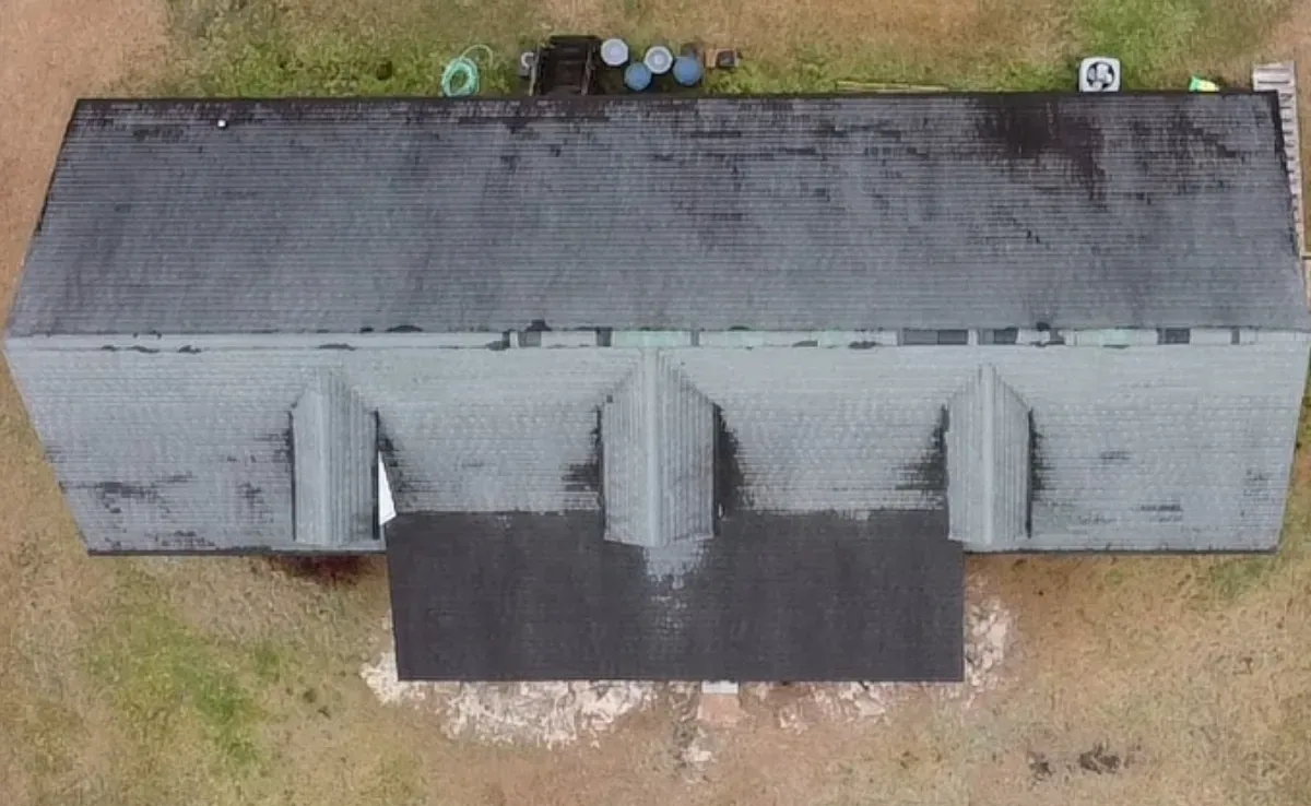 Drone image of a deteriorated shingle roof on a Wilmington NC home, showing widespread wear, missing granules, dark staining, and weakened areas around dormers prior to installing a new 24-gauge double-lock standing seam metal roofing system.