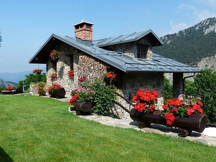 A stone house with a chimney and flowers in front of it. A stone house with a chimney and flowers in front of it
