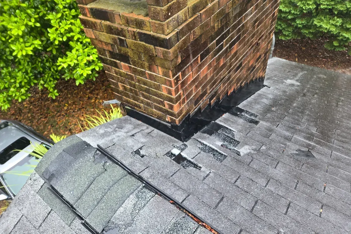 Roof repair services before photo in Wilmington NC showing damaged shingles and worn chimney flashing prior to repair.