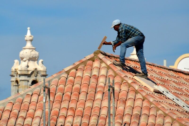A man is working on the roof of a building with a hammer. A man is working on the roof of a building with a hammer.