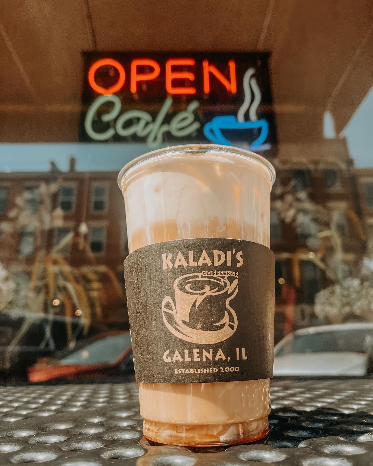 A cup of coffee is sitting on a table in front of an open cafe sign.