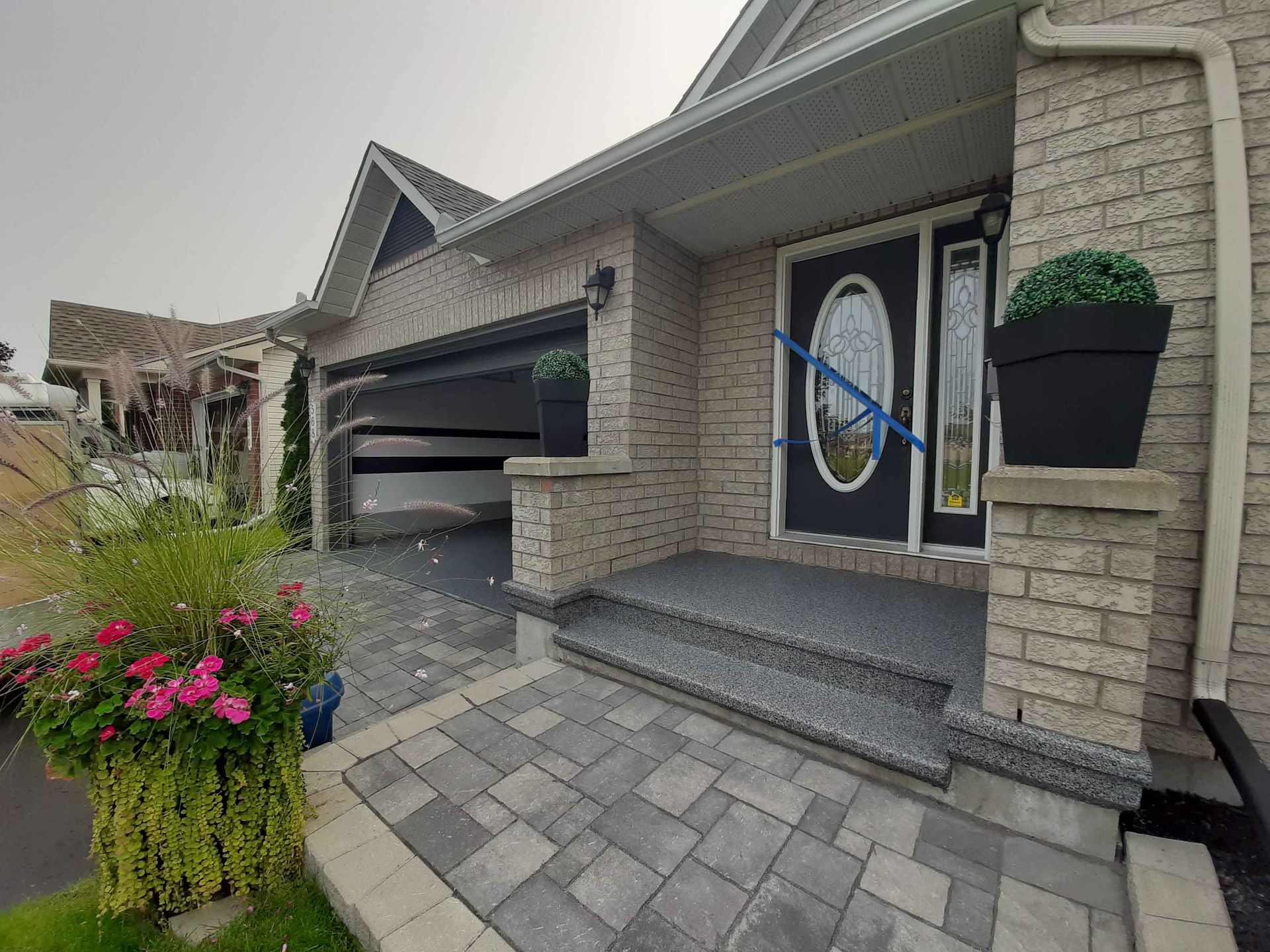 Une maison en briques avec une porte noire et une allée en briques qui y mène.