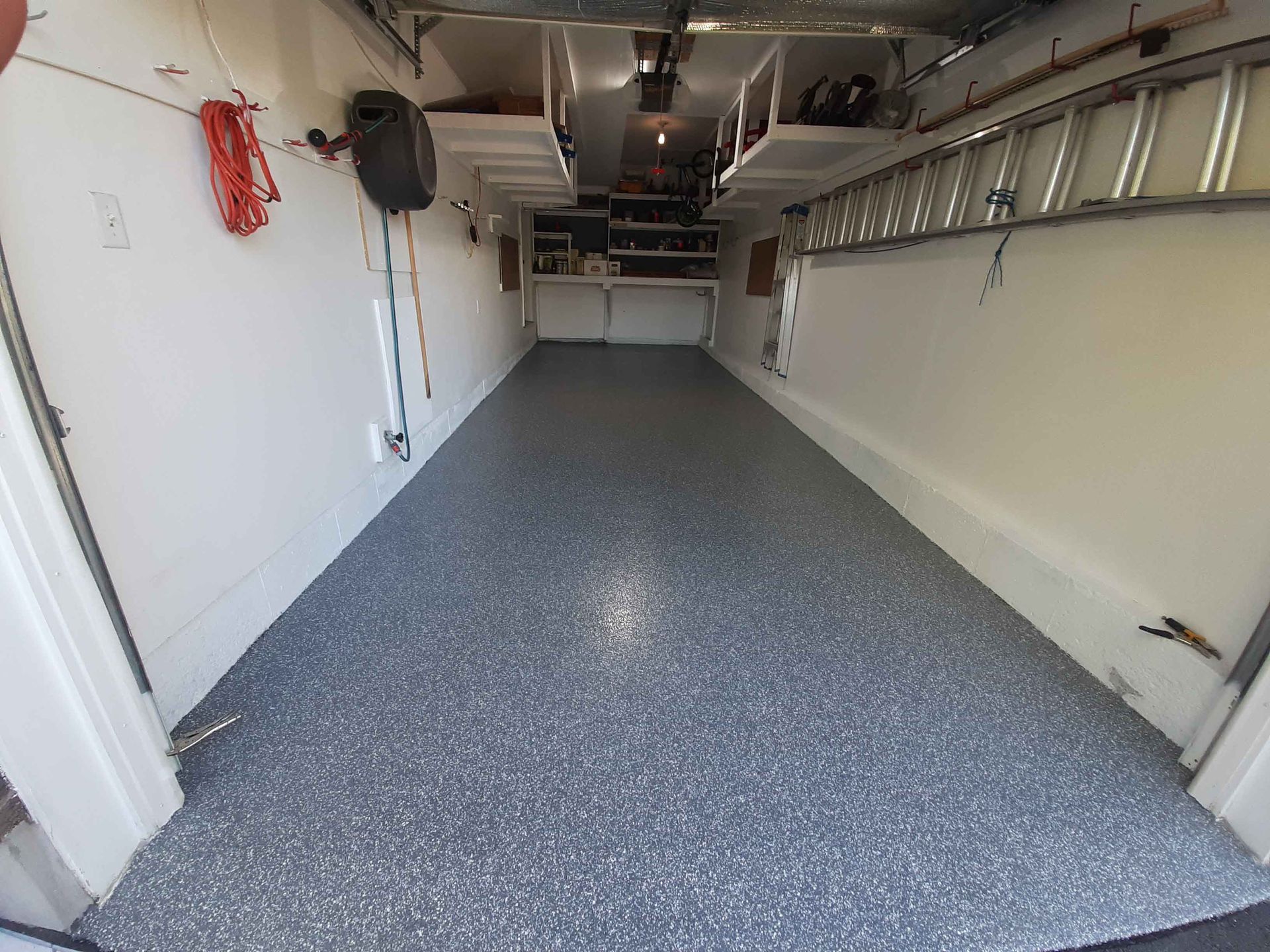 Un garage avec une échelle suspendue au plafond et un sol gris.