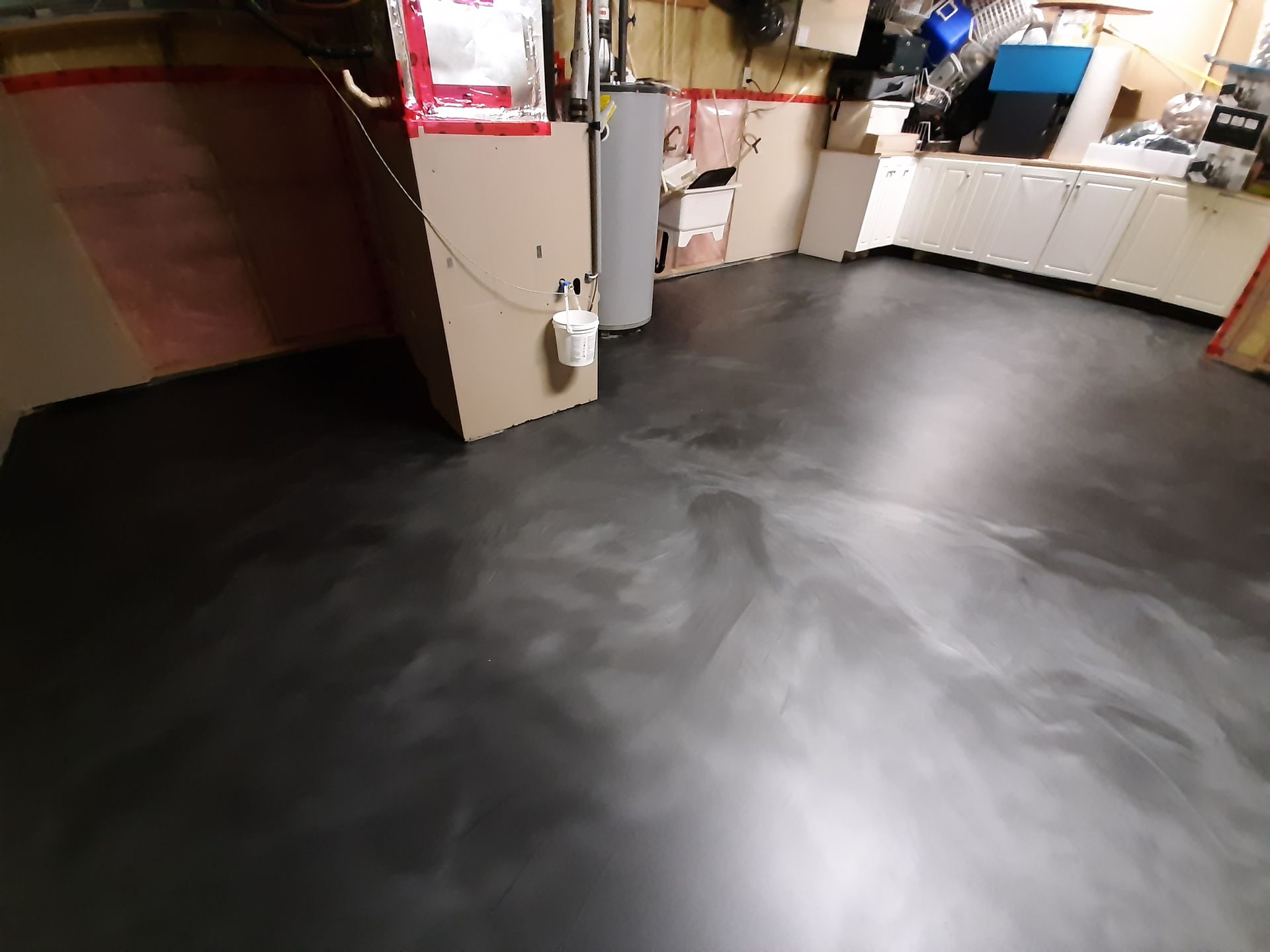 Une pièce avec un sol noir et un seau sur le mur.