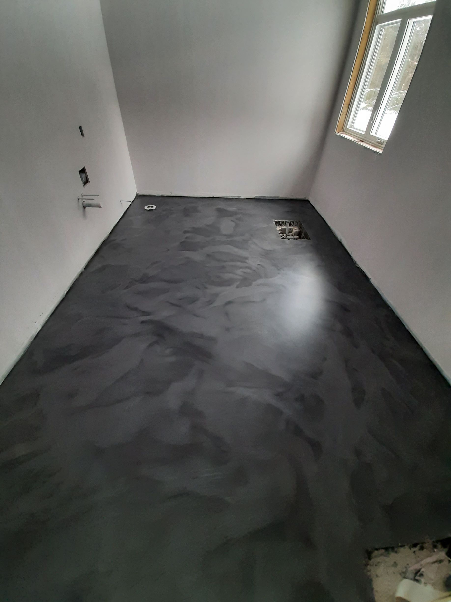 Une pièce avec un sol noir et une fenêtre.