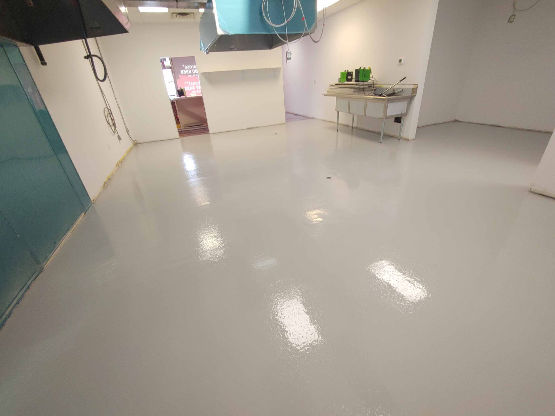 A large empty room with a white floor and a sink.