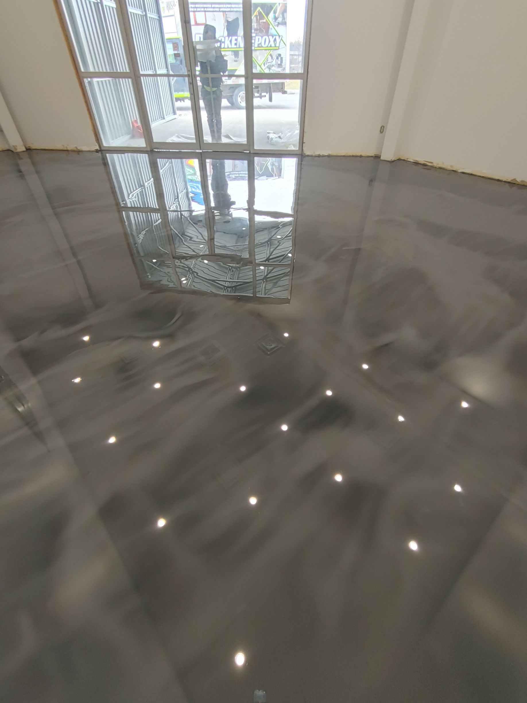 Une personne se tient dans une pièce avec un sol brillant et une fenêtre.