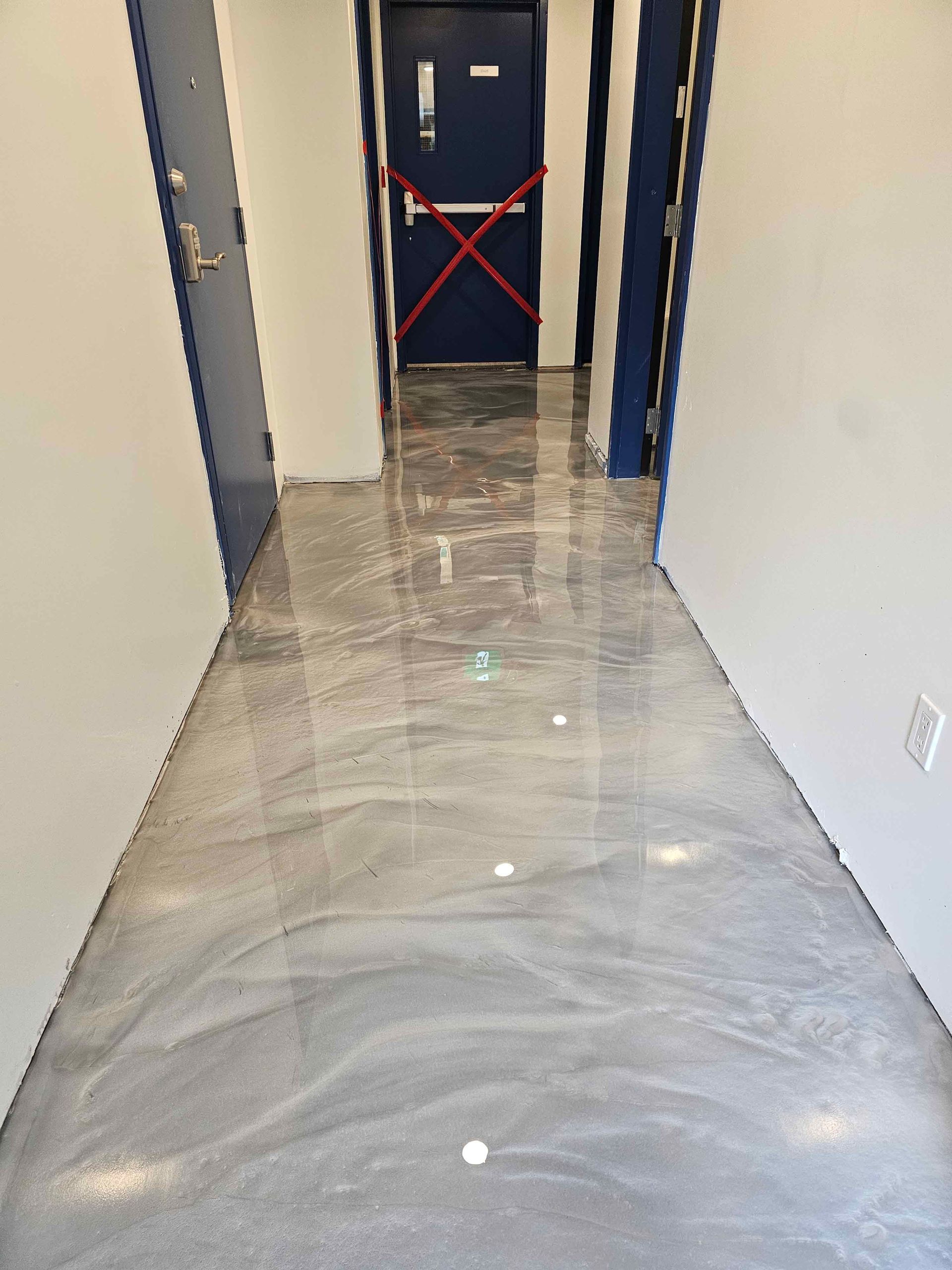 Un couloir avec un sol métallique brillant et une porte bleue.
