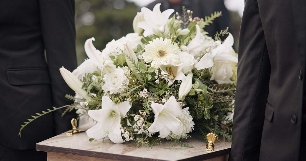 Una bara piena di fiori bianchi viene trasportata da due uomini.