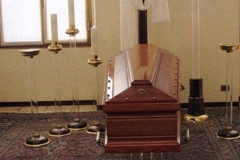 Una bara di legno si trova in una stanza circondata da candele