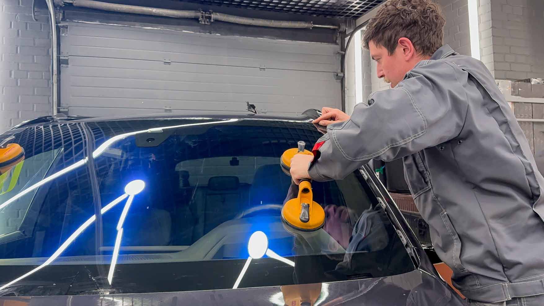 Technician replacing the windshield of a car in an auto service station garage with suction cups.