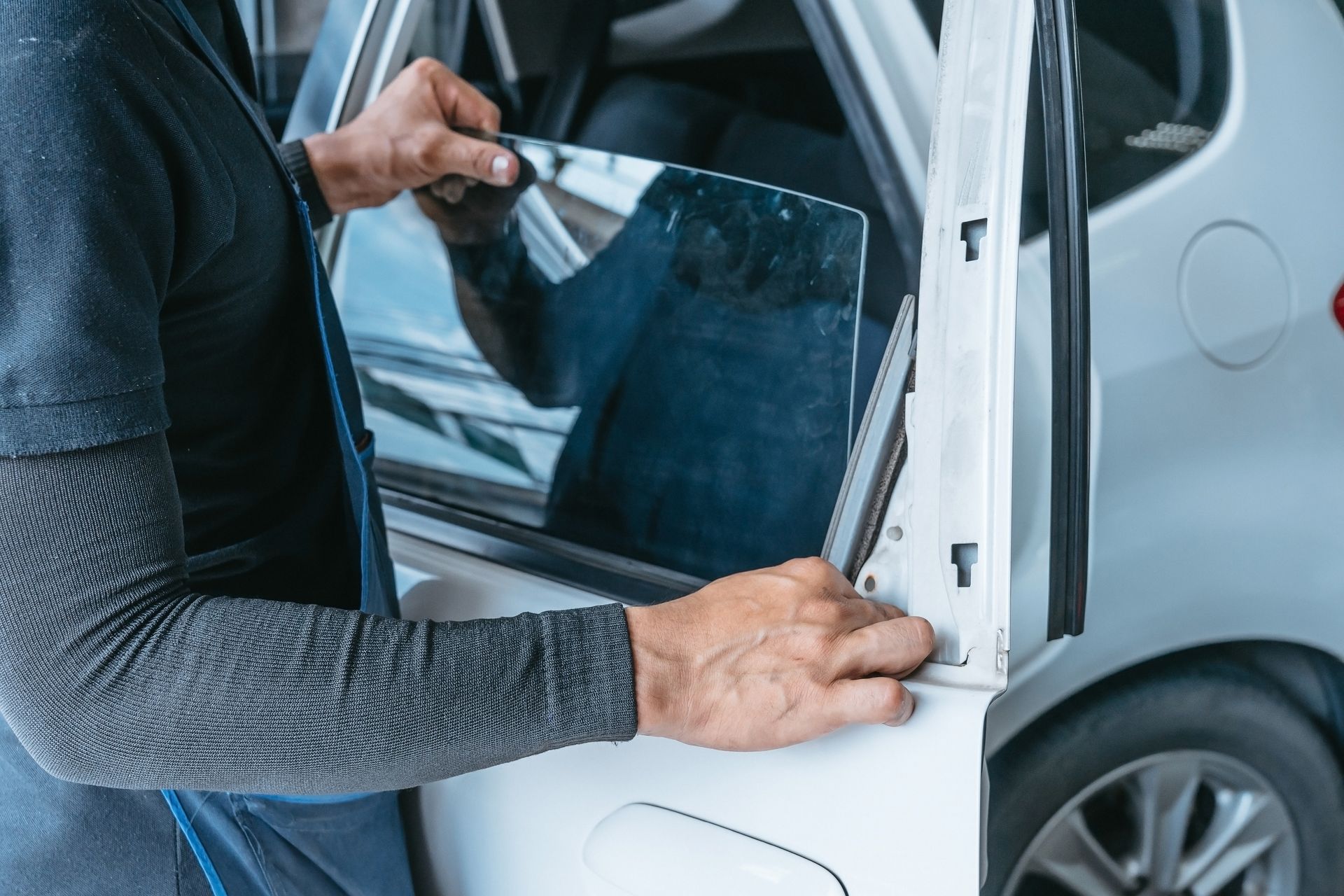 Unrecognized worker performing a car window replacement job on a white car in an auto repair shop.