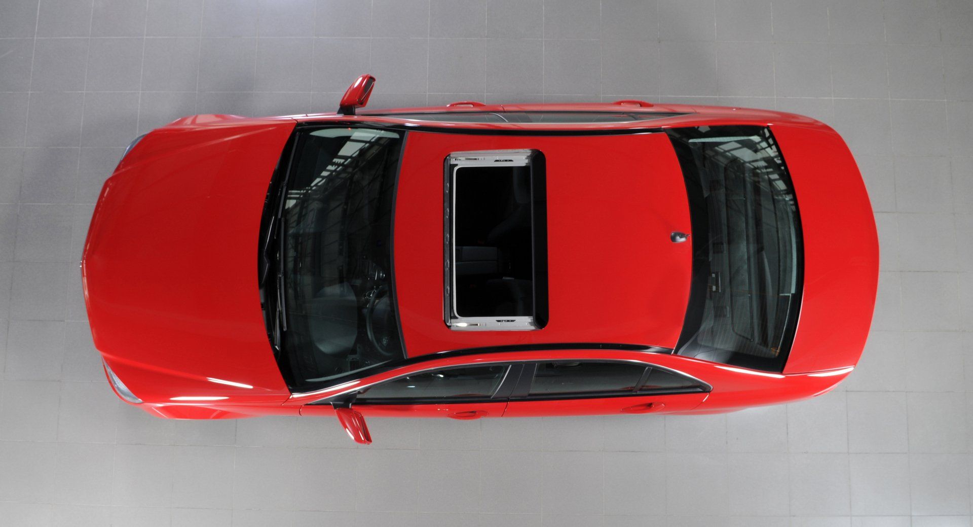 Overhead view of a red car with an open sunroof. A white phone sits on the car's roof.