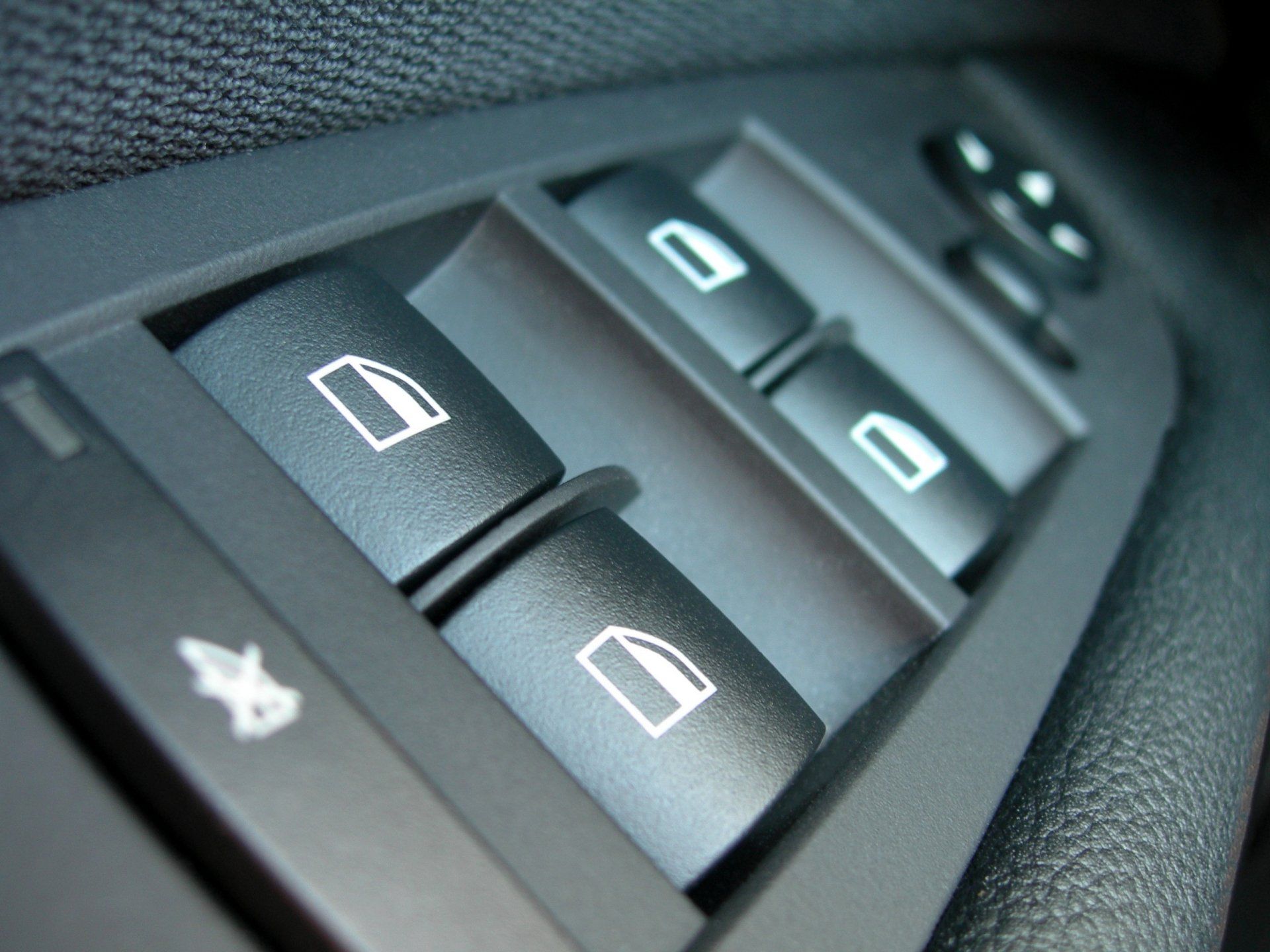 Close-up of car window control panel with black buttons featuring window icons and a lock symbol.