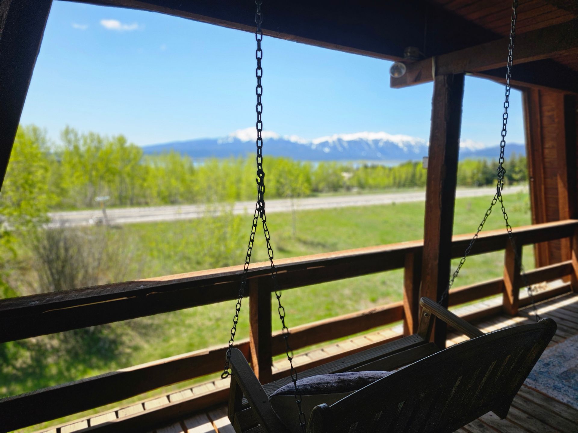 Porch swing overlooking a road and mountain range, blue sky.