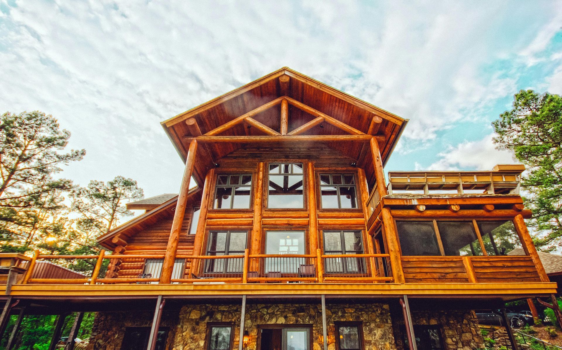 Log cabin with wooden exterior, stone foundation, and large windows under a cloudy sky.