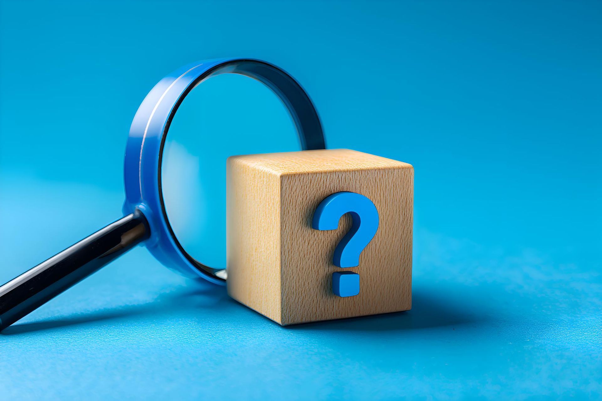 Magnifying glass over a wooden cube with a blue question mark on a blue surface.