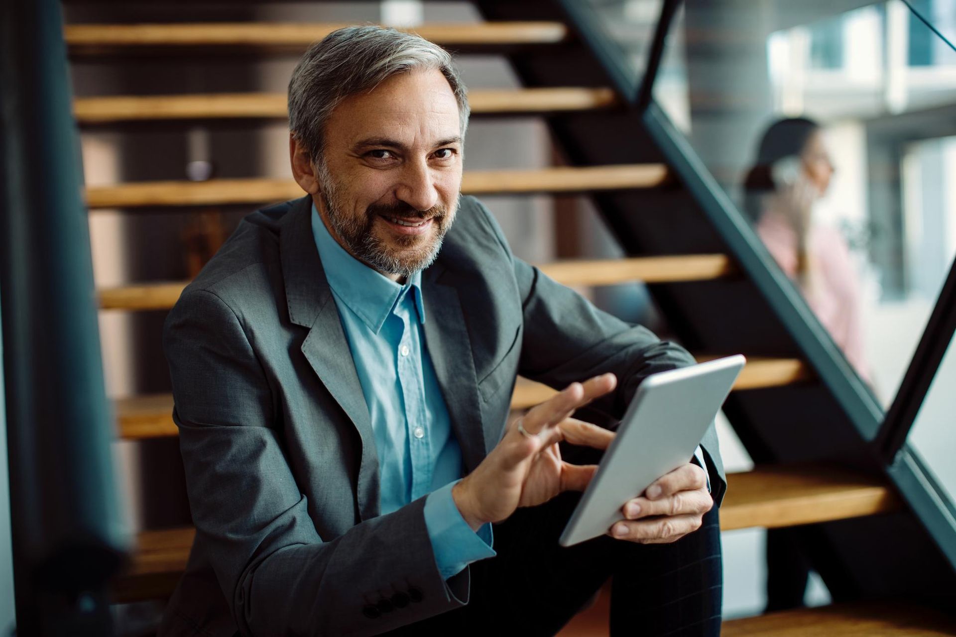 A man is sitting on a set of stairs using a tablet computer.