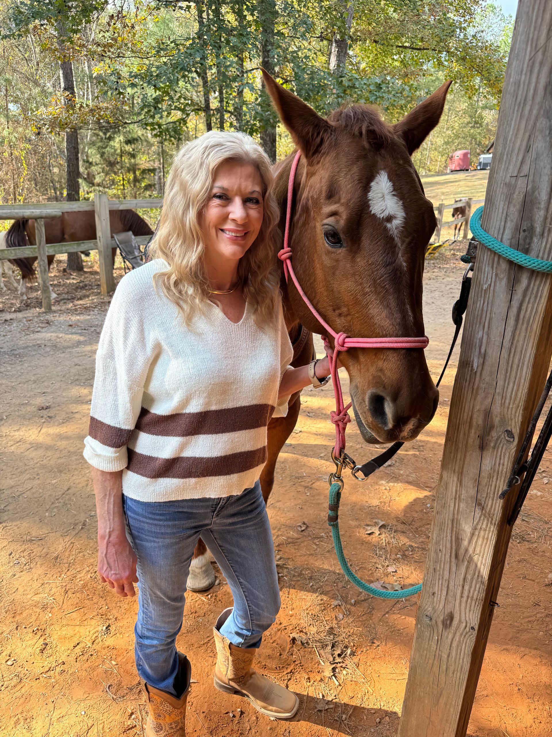 A woman in a red jacket is standing next to a brown horse.