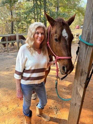 A woman in a red jacket is standing next to a brown horse.