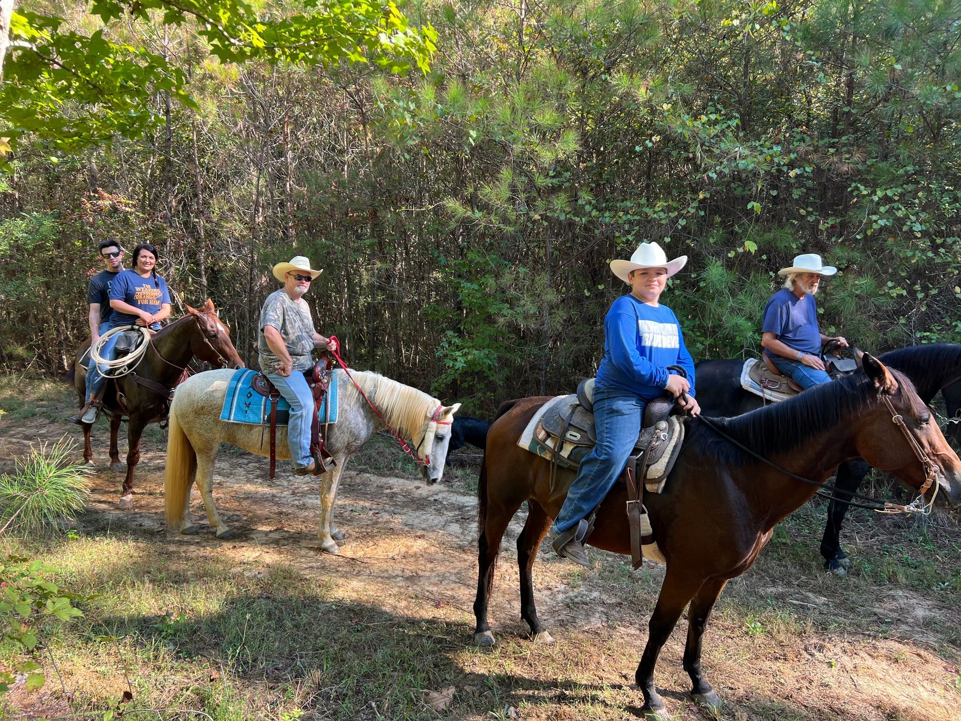 Group of people riding horses on a wooded trail, all wearing cowboy hats.