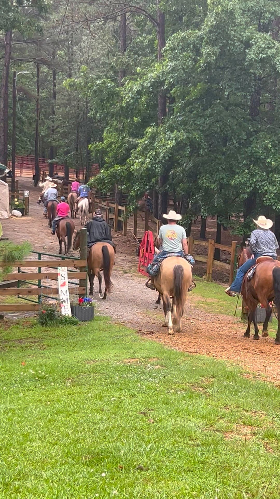 A group of people on horseback riding down a dirt path lined with trees and greenery.