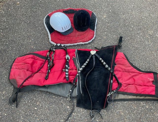 Horse riding gear: red saddle pad, black bridle, helmet, and breastplate on asphalt.