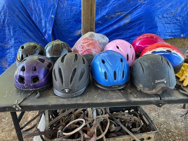 A collection of riding helmets of various colors on a table, with a blue tarp background.