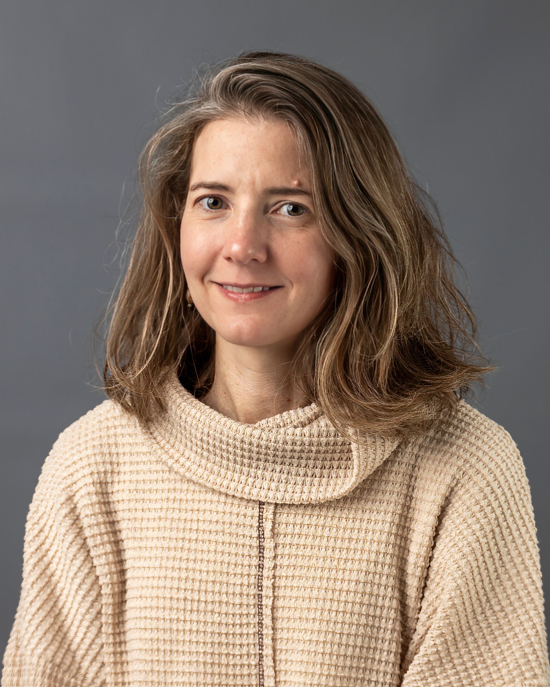 a woman in a tan sweater is smiling for the camera .
