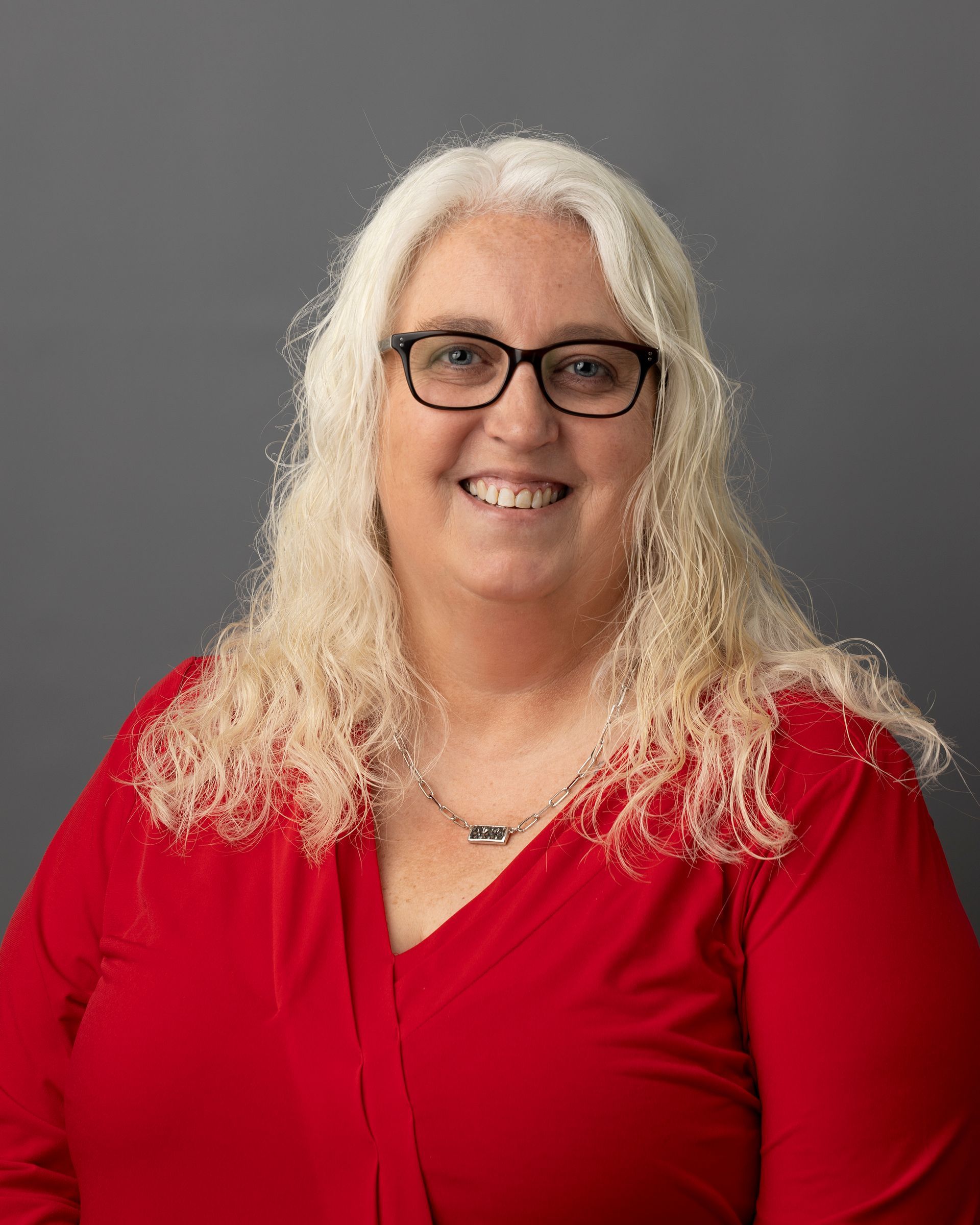 a woman wearing glasses and a red shirt is smiling for the camera .