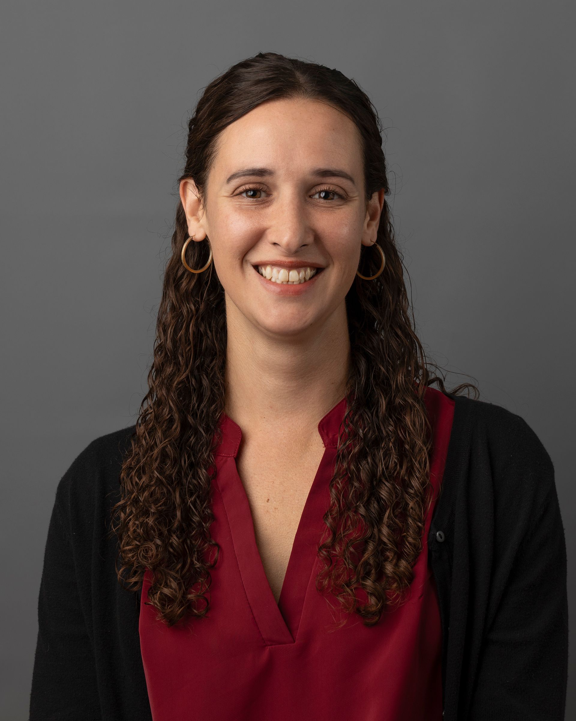 a woman wearing a red shirt and a black sweater is smiling for the camera .