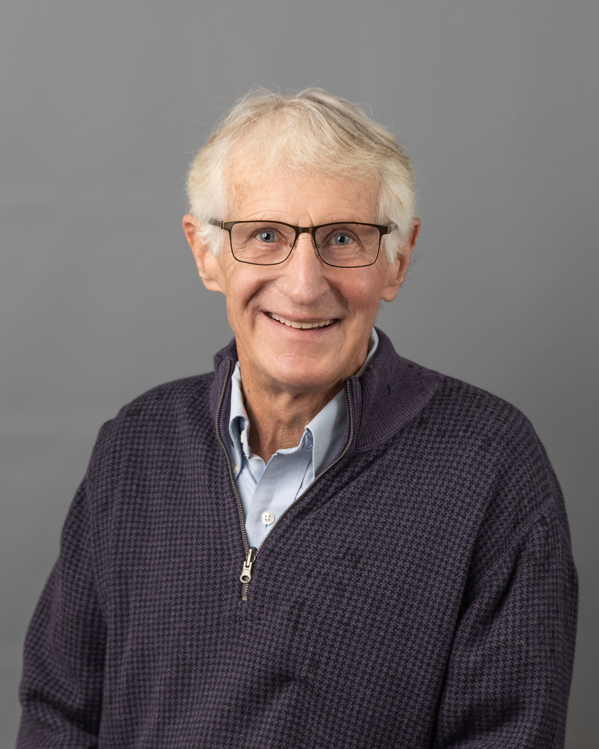 a man wearing glasses and a purple sweater is smiling for the camera .