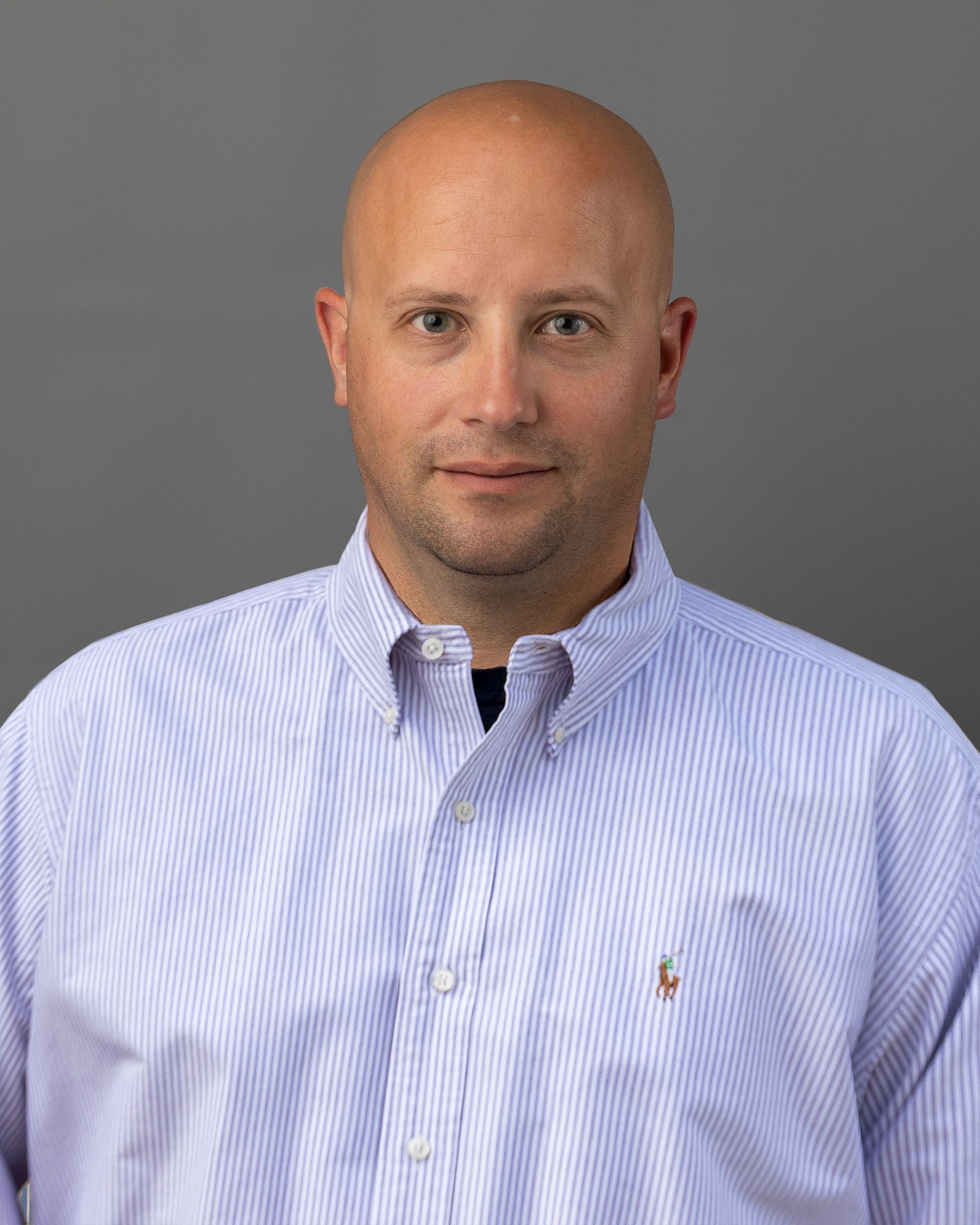 a bald man wearing a striped shirt is standing in front of a gray background .