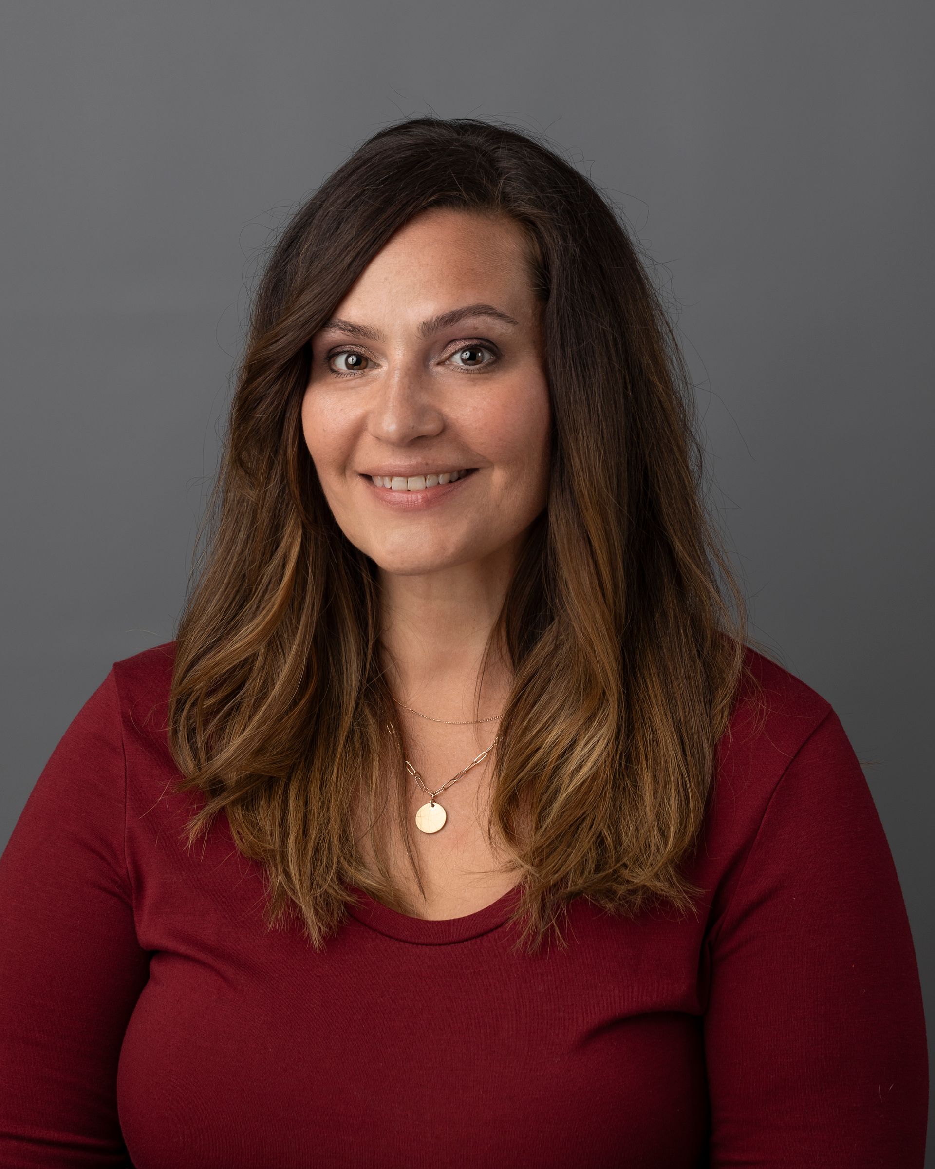a woman wearing a red shirt and a necklace is smiling for the camera .