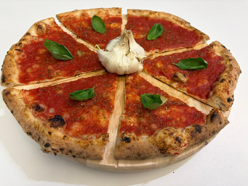 Pizza tagliata a spicchi, condita con salsa rossa, foglie di basilico e una testa d'aglio.